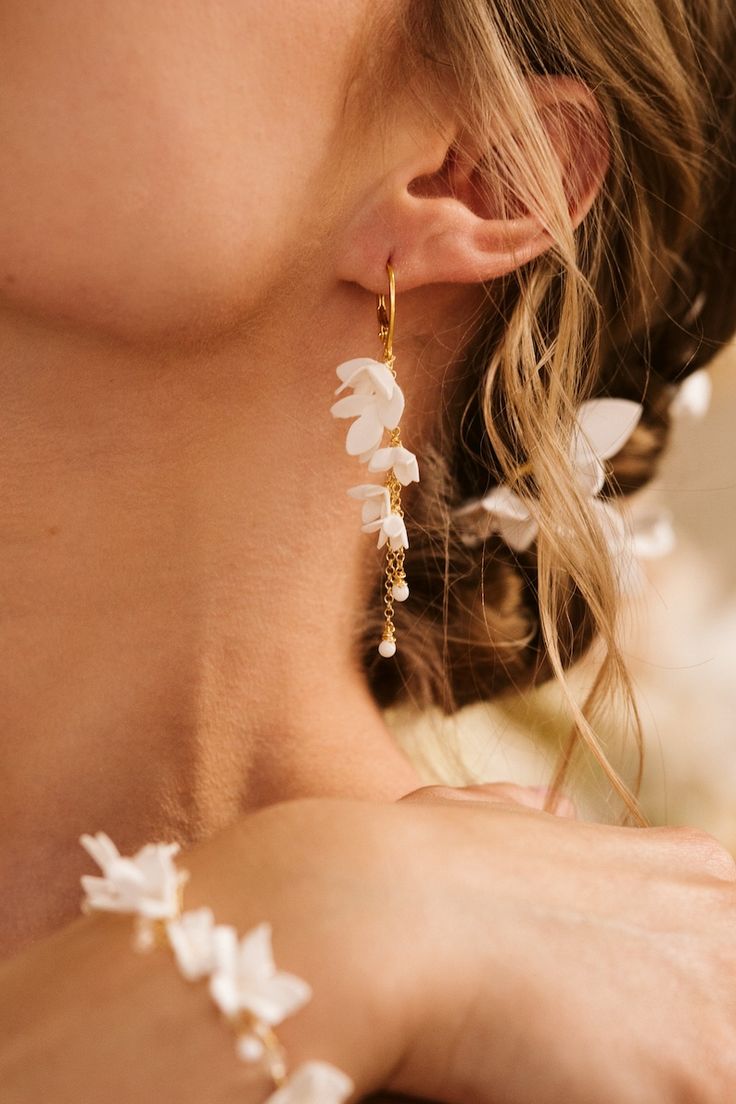 a close up of a person wearing white flowers on her ear and necklace with gold chains