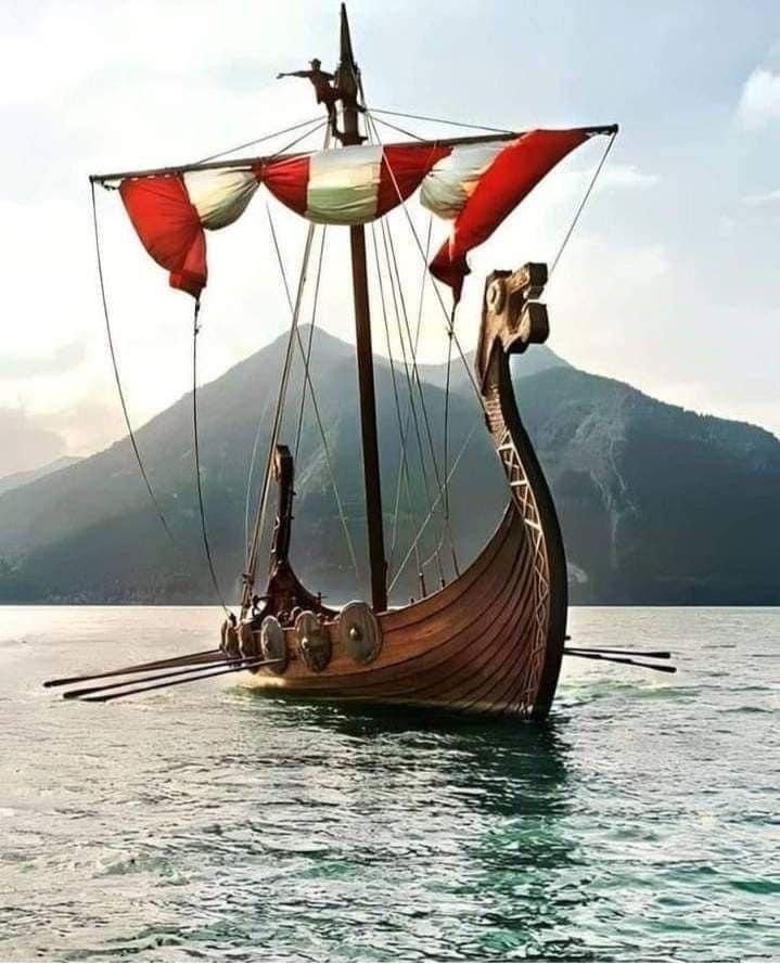 an old wooden boat with red sails floating on the water in front of some mountains