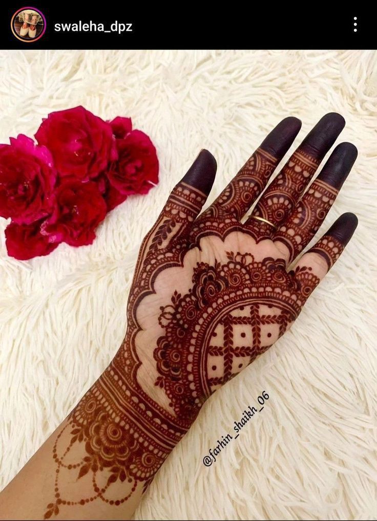 a henna on someone's hand with red flowers in the background and white furnishing