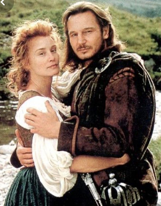 a man and woman dressed in period clothing standing next to each other near a river