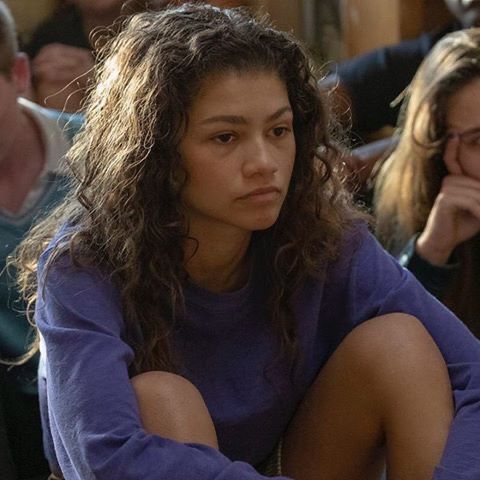 a woman sitting on the ground in front of a group of people with their arms crossed