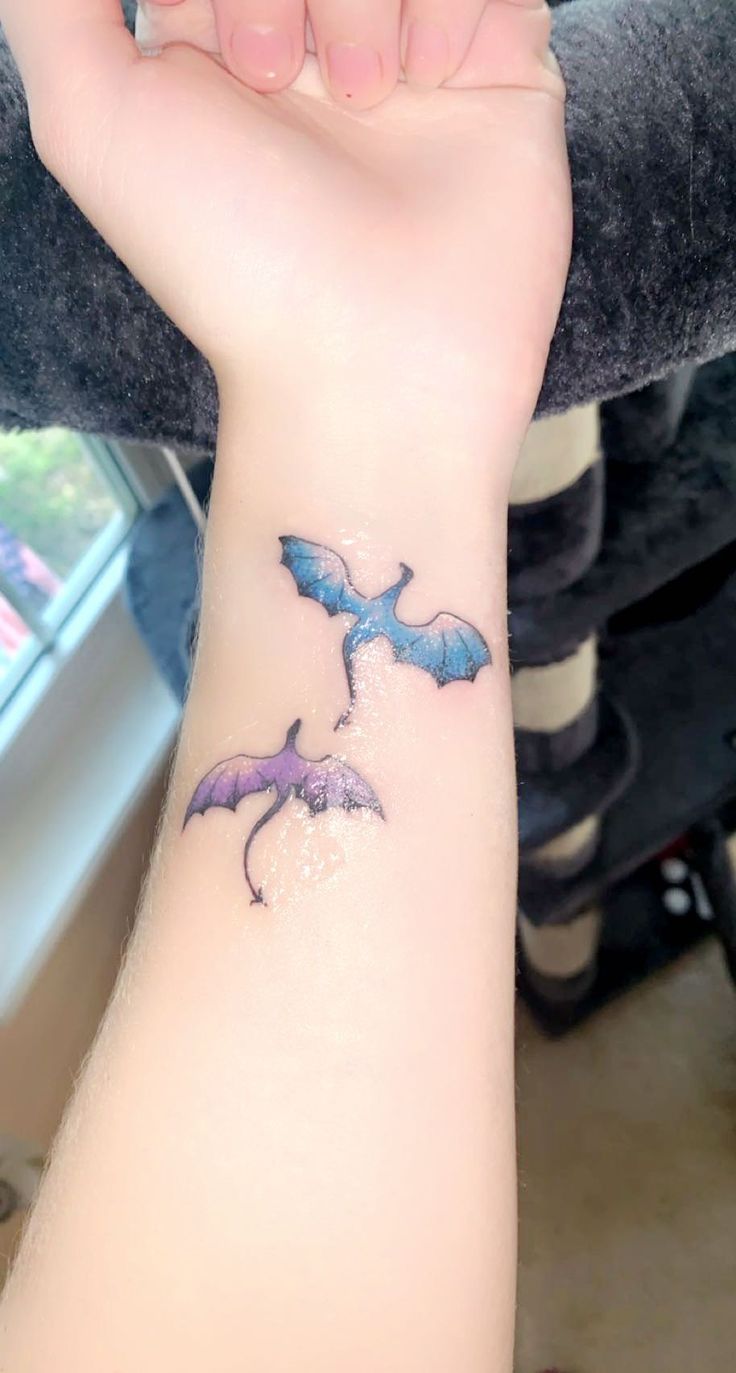 a woman's arm with a tattoo on it that has two purple bats flying through the air