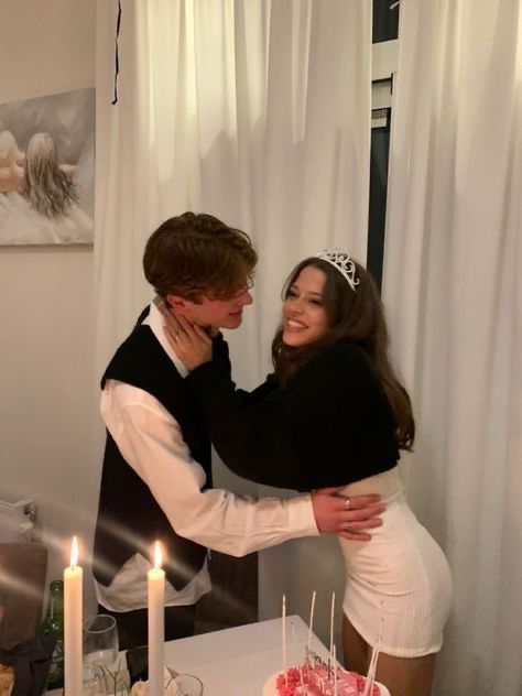 a young man and woman hugging in front of a cake with candles on it at a party