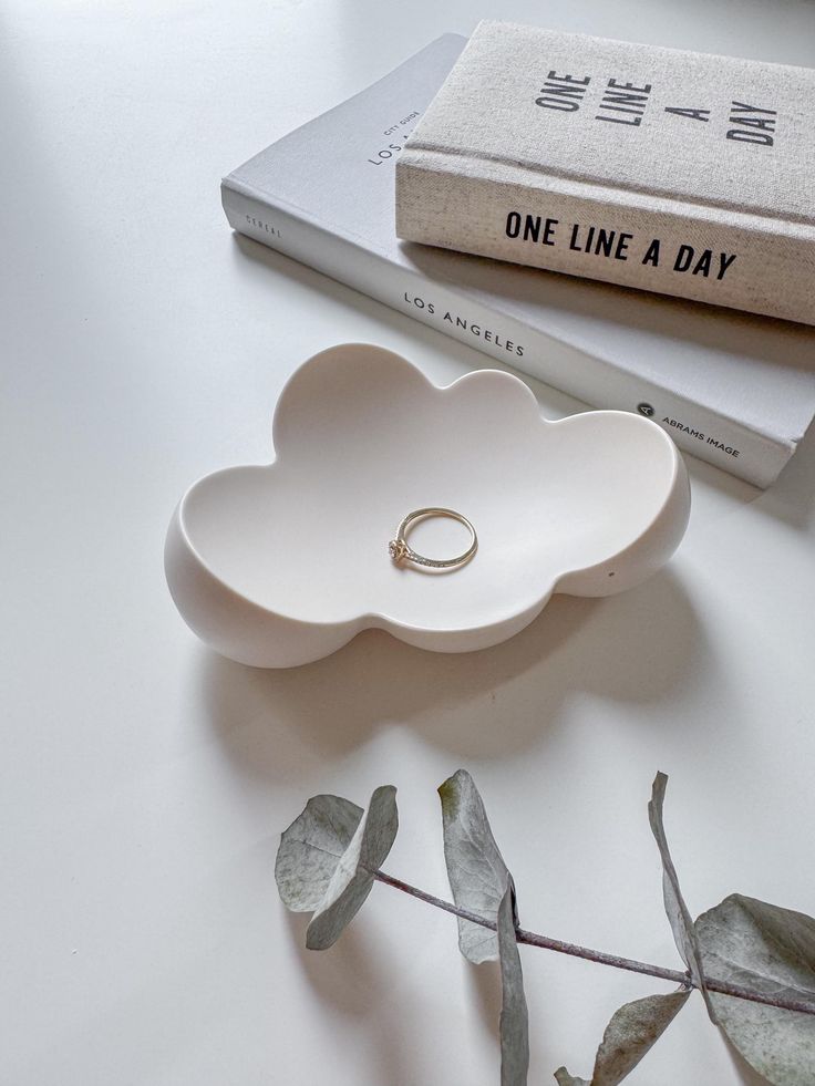 a ring dish sitting on top of a table next to a book and some leaves