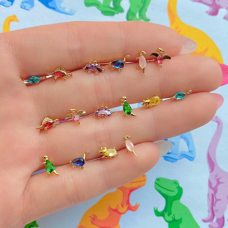 Let's go back in time in the Dino-Mite Stud Set! We love how fun these dinosaur studs are and they'll definitely add so much personality to any outfit! 18k gold plated, 18k rose gold plated, or rhodium plated over brass Cubic zirconia stones Approx. 4mm wide Sterling silver posts and butterfly backings Four mismatched Dinosaur Dance, Beautiful Trinkets, Dinosaur Stuff, Ear Stacks, Trinkets Jewelry, Character Customization, Ear Curation, Paintings Tutorials, Dinosaur Necklace