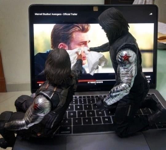 two toy figures sit on top of a laptop computer screen, facing each other and touching noses