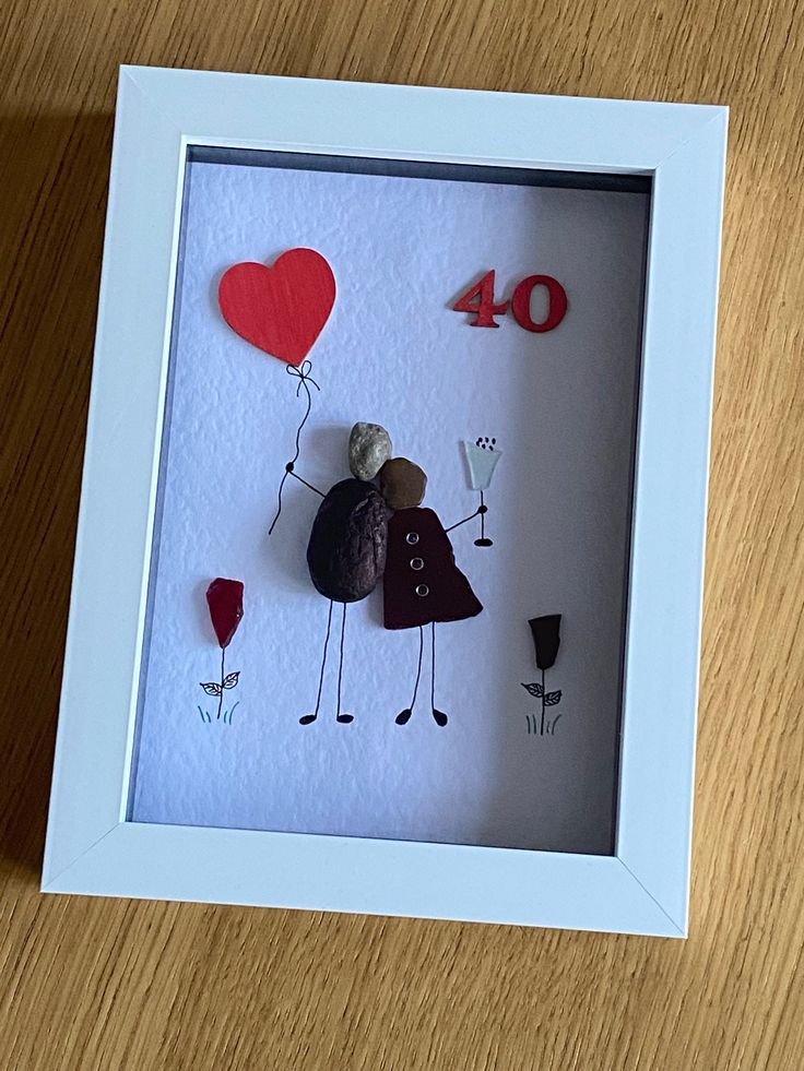 a white frame with some red and black items in it on a wooden table next to a cell phone