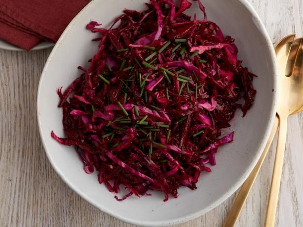 a white bowl filled with red cabbage and gold spoons next to a napkin on top of a wooden table