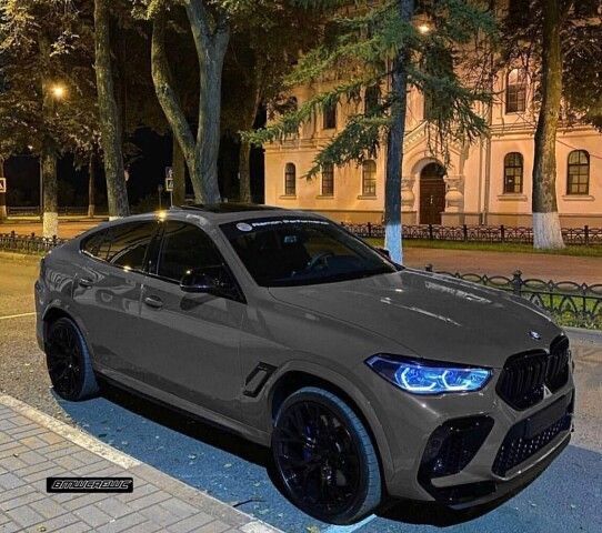 a grey bmw suv parked on the side of a road at night with trees in the background