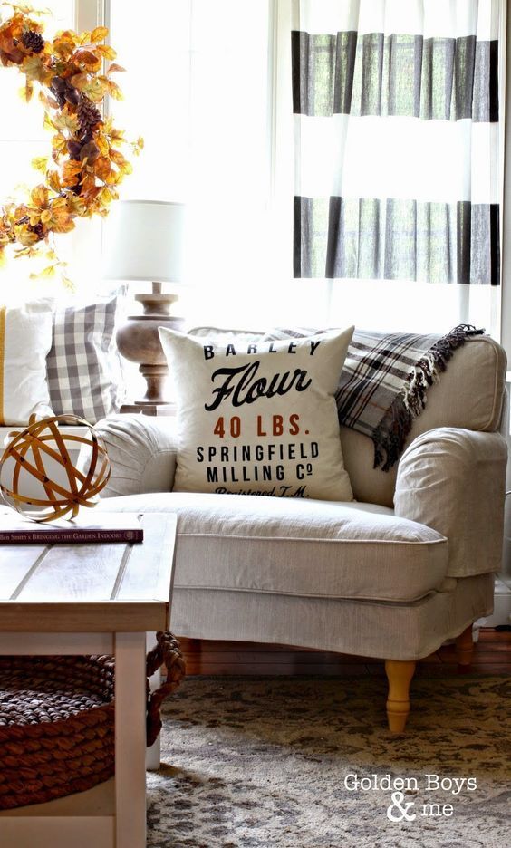 a living room with white couches and pillows on top of the couch, in front of a window