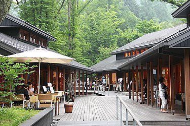 people are sitting at tables in front of some wooden buildings with umbrellas over them