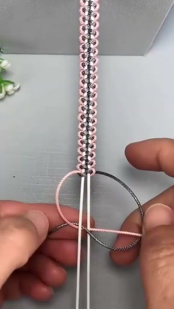 someone is making a string with pink beads and white thread on the end, while another person's hands are holding it