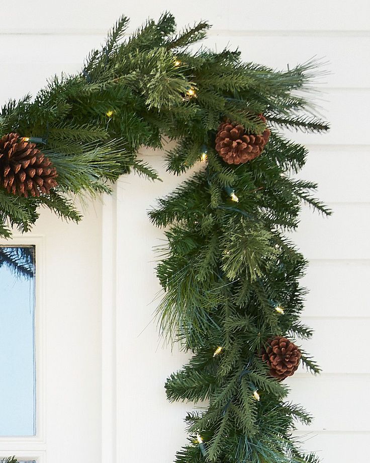 a wreath with pine cones and lights hanging from the side of a white house door