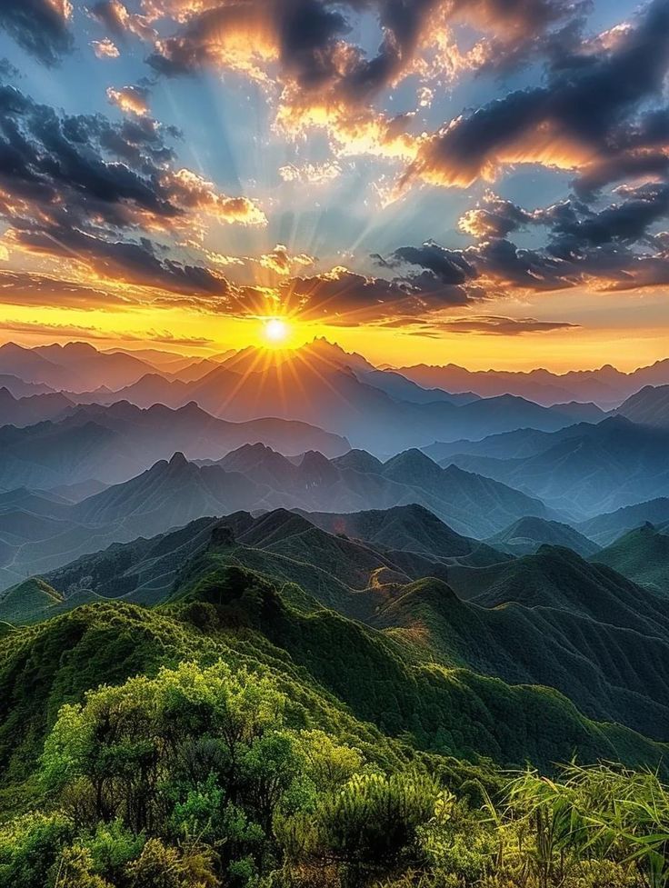 the sun is setting over mountains with green trees and bushes on top, in the foreground