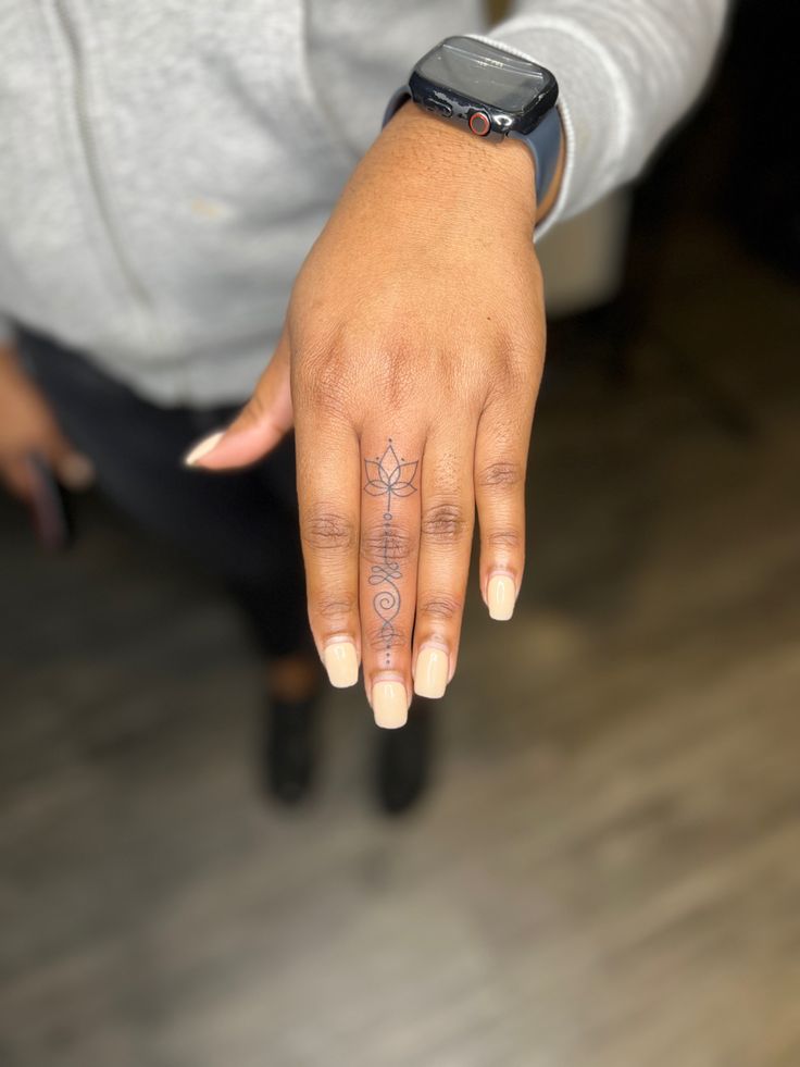 a woman's hand with a tattoo on her left thumb and an apple watch in the background