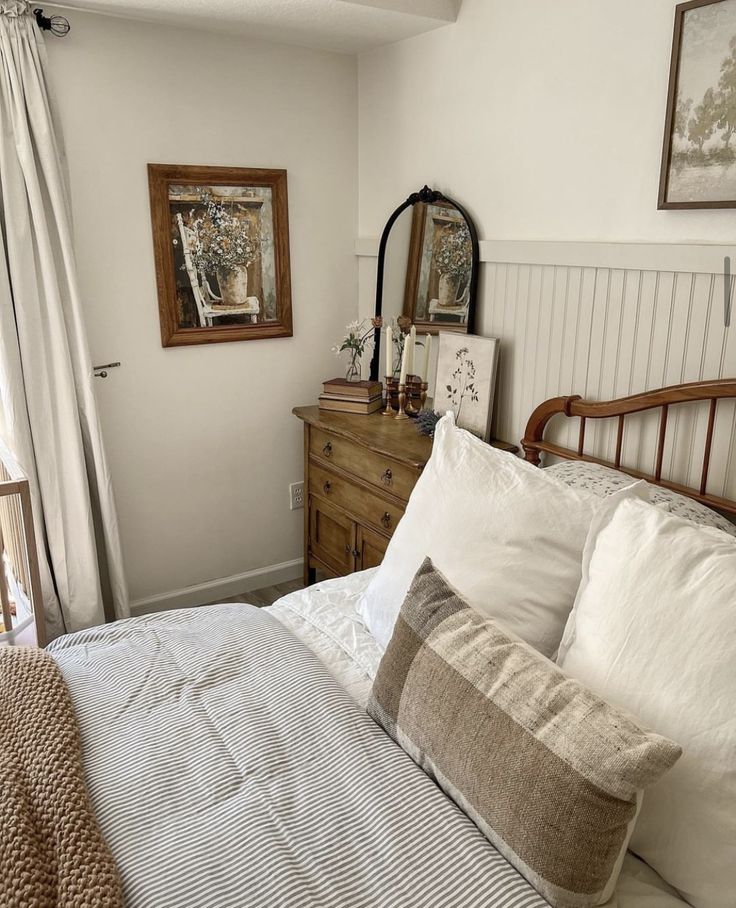 a bed with white sheets and pillows in a bedroom next to a dresser, mirror and pictures on the wall