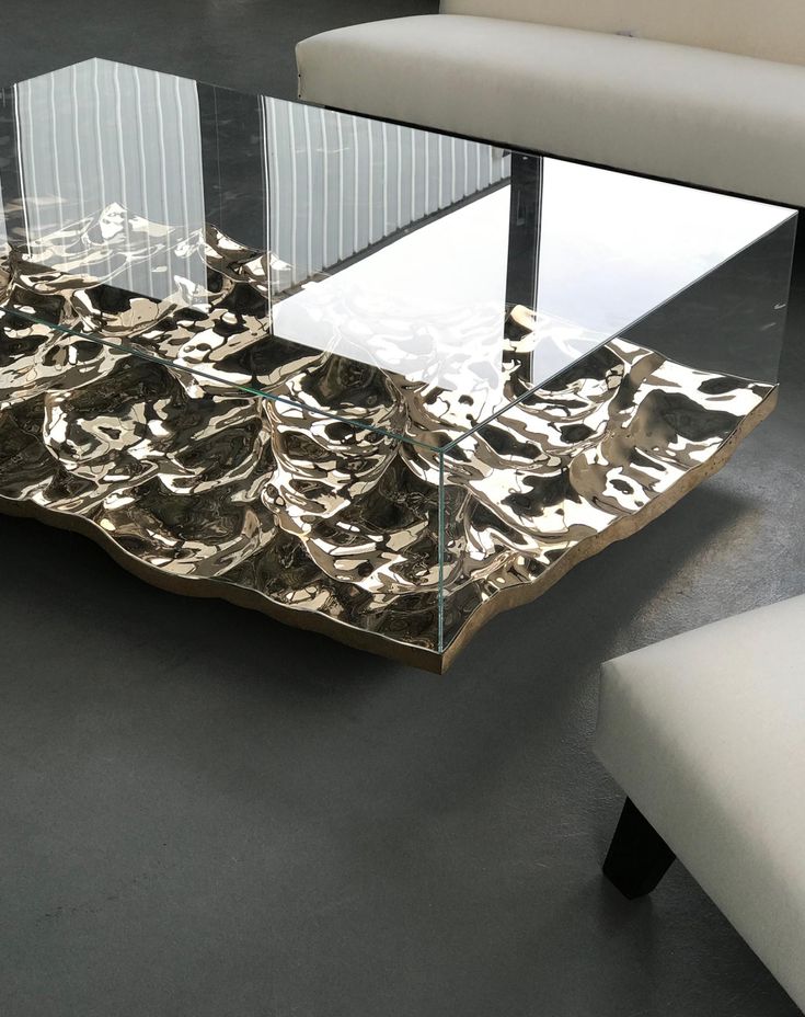 a glass and metal coffee table sitting on top of a gray floor next to a white chair