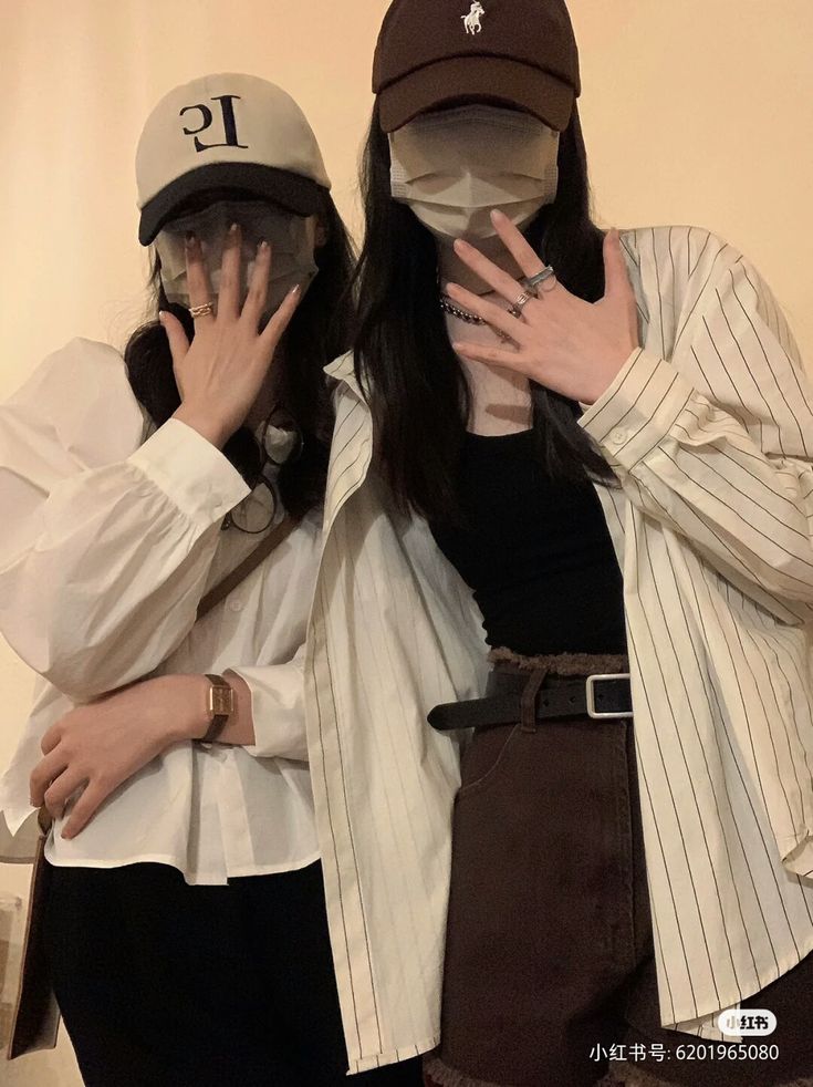 two people wearing hats and holding their hands to their faces while standing next to each other