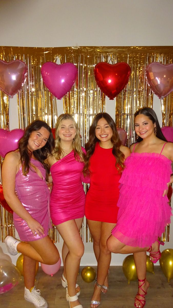 four women in pink and red dresses posing for the camera with heart balloons behind them