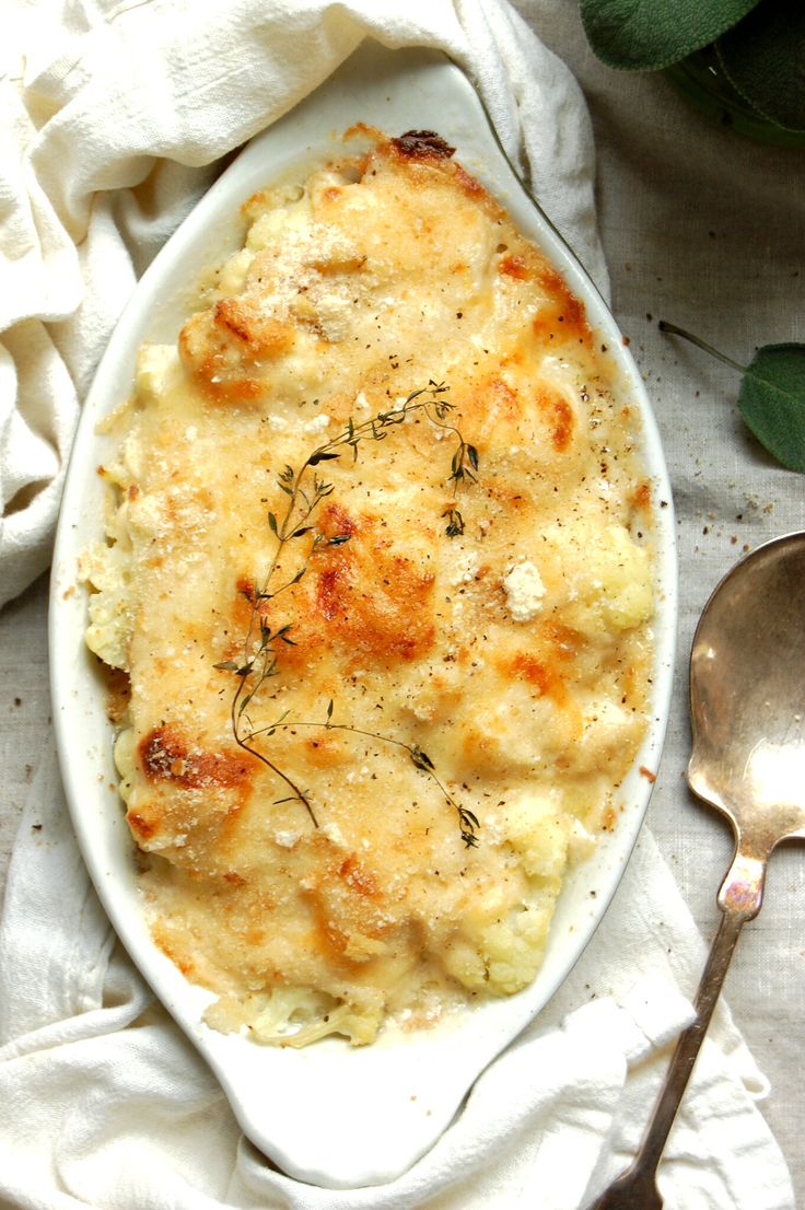 a white dish filled with macaroni and cheese on top of a table next to a spoon