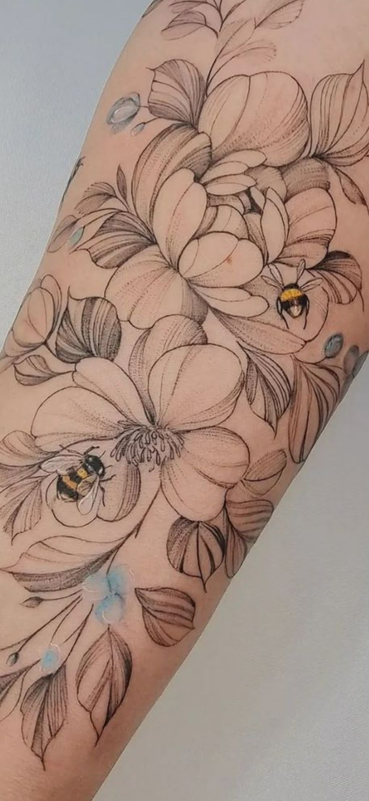 a close up of a person's arm with flowers and bees on the side