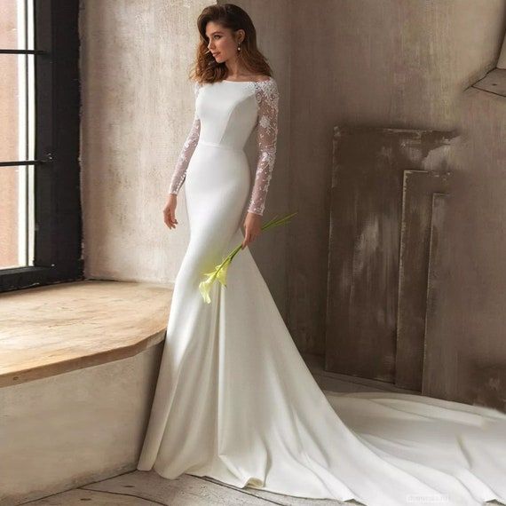 a woman in a white wedding dress leaning against a window sill with her hands on her hips