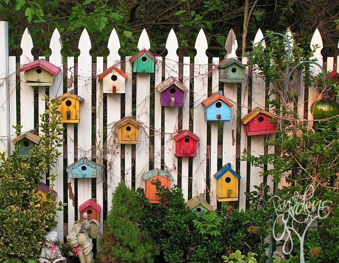 colorful birdhouses on a white picket fence