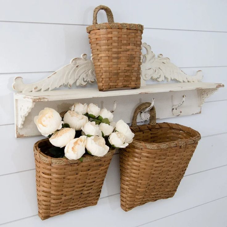 two wicker baskets are hanging on the wall with white flowers in them and one has a bird perched on it