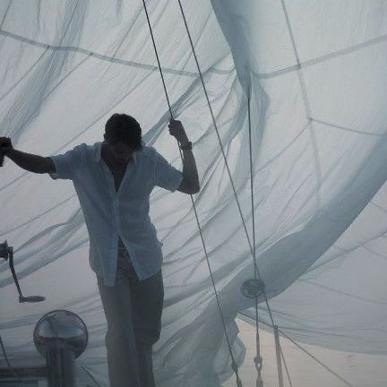 a man standing on top of a boat next to a white sheet covering the sails