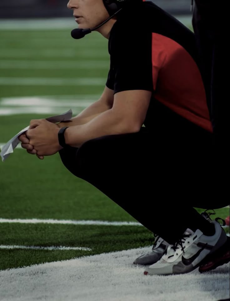 a football player sitting on the sidelines with his headphones up to his ear