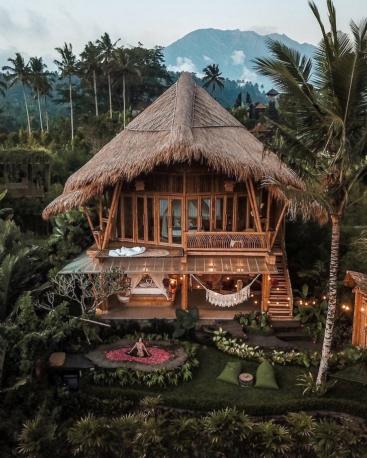 an aerial view of a wooden house surrounded by trees and greenery with lights strung from the roof