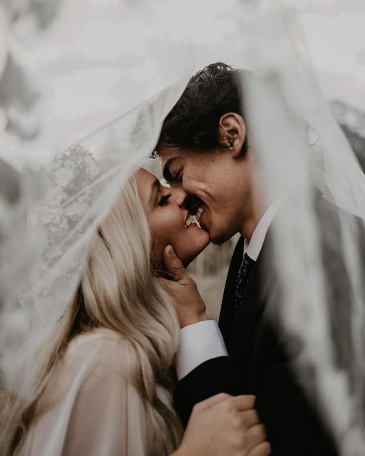 a bride and groom kissing under the veil on their wedding day in an outdoor setting