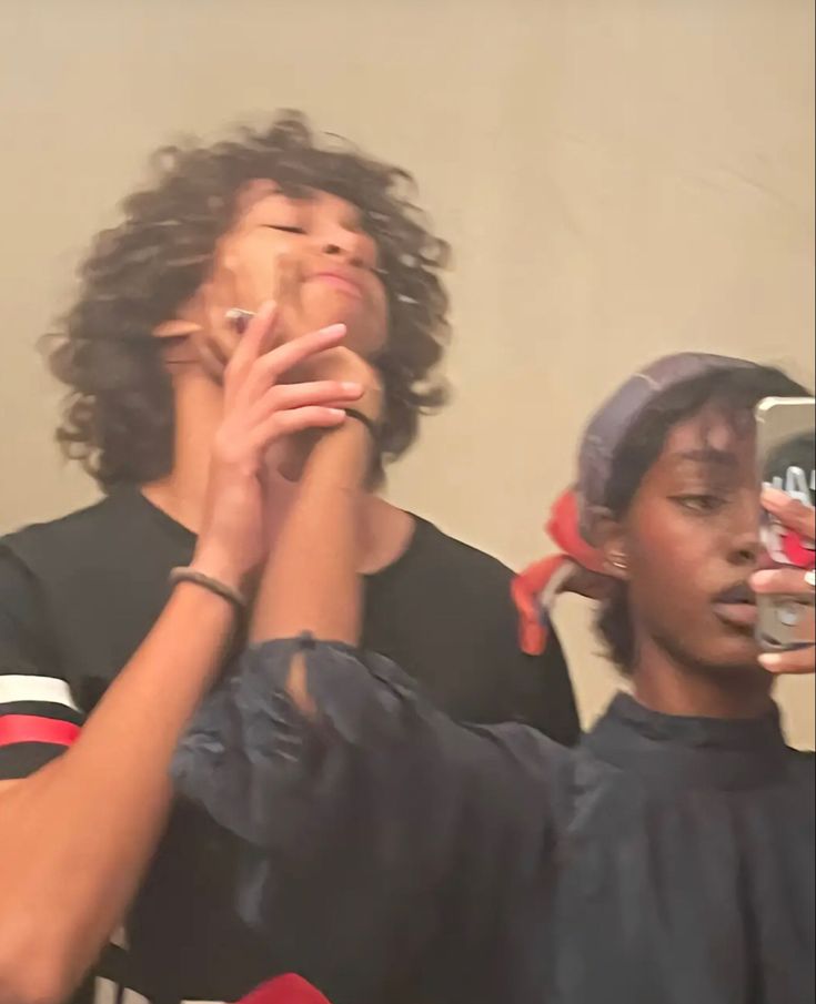 two people standing next to each other with their hands on their faces and one holding something in the other hand