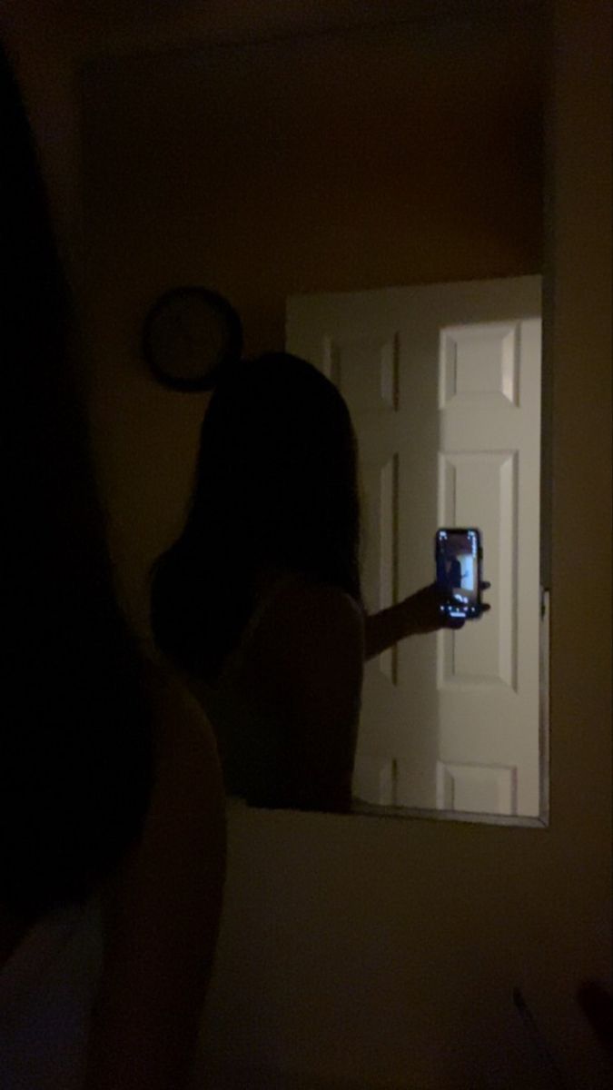 a woman taking a photo of herself in the mirror with her cell phone at night