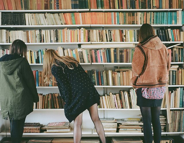 three women standing in front of a bookshelf with many books on the shelves