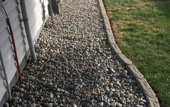 a gravel path next to a house with grass and bushes on the side of it