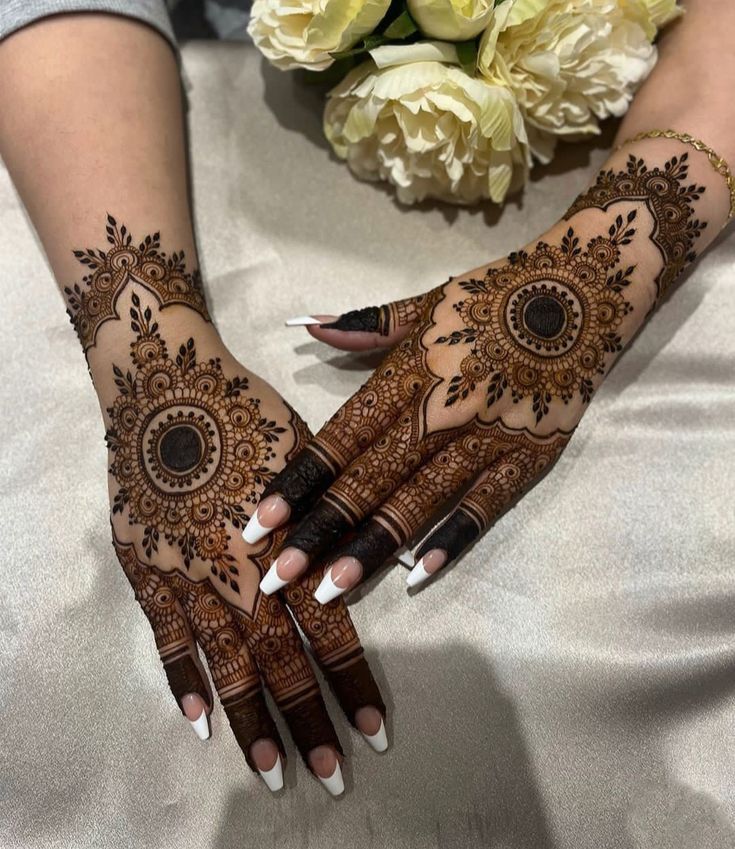 two hands with henna designs on them, one is holding flowers and the other is sitting