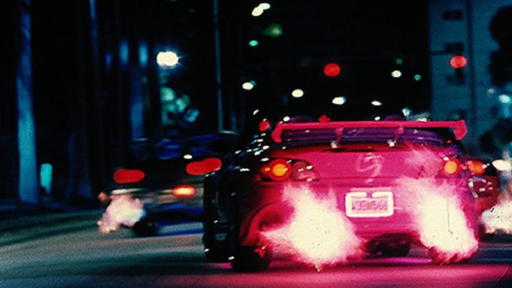 the back end of a red car driving down a street at night