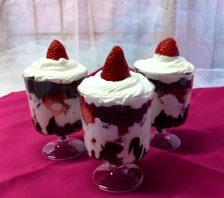 three dessert cups with strawberries and whipped cream in them on a pink table cloth