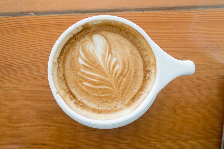 a cappuccino in a white cup with a leaf design on the foam