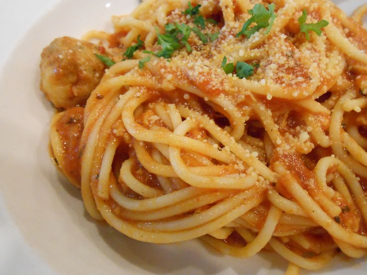 a plate of spaghetti with meatballs and parmesan cheese on the top is ready to be eaten