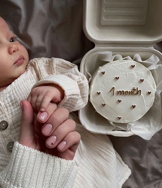 a woman holding a baby in her arms next to a cake with the word i month written on it