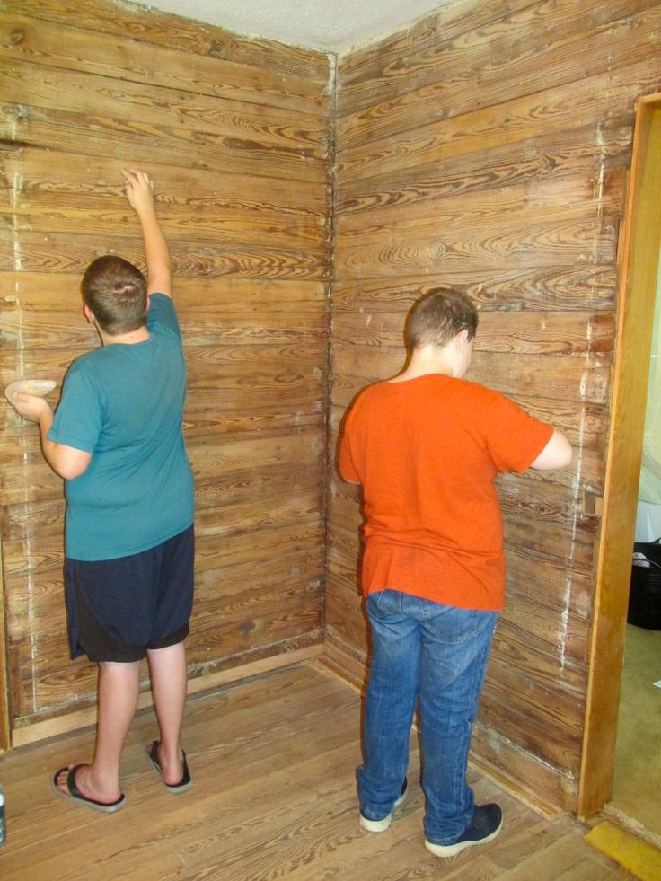 two people are standing in the corner of a room that has wood paneling on it