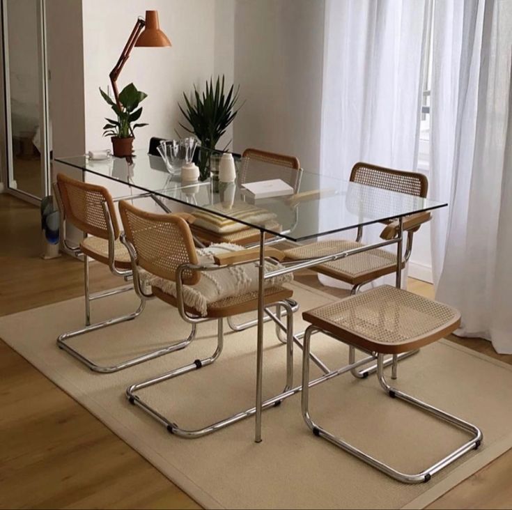 a glass dining table with four chairs and a potted plant on the far side