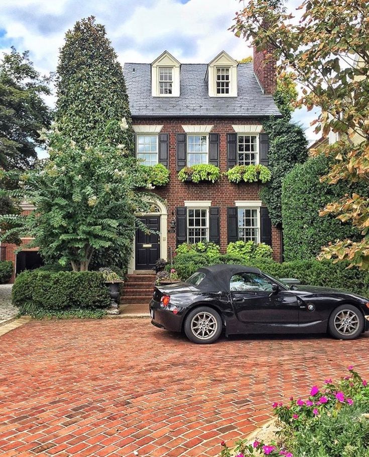 a black sports car parked in front of a large brick house with ivy covered windows