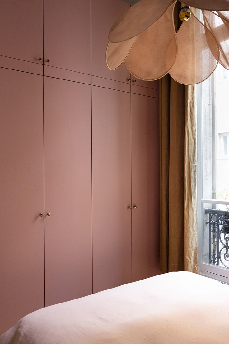 a bedroom with pink walls and white bedding, hanging lamp over the headboard