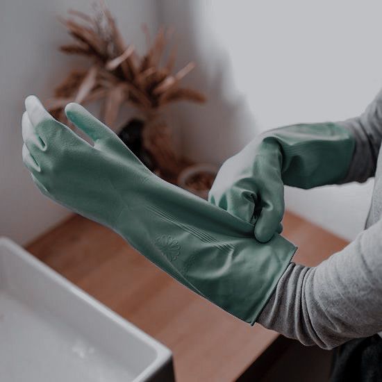 a person wearing green gloves in front of a sink with a wooden table and plant