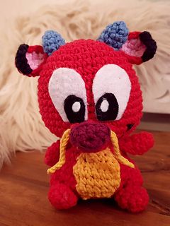 a crocheted red stuffed animal sitting on top of a wooden table