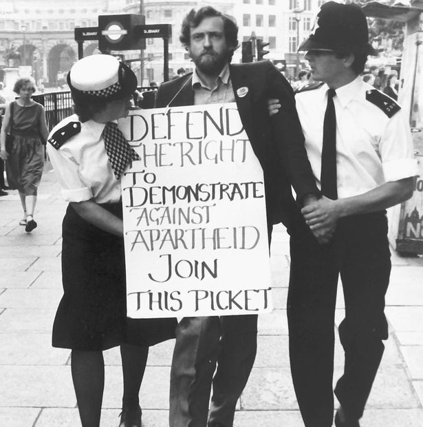 two police officers holding a protest sign on the sidewalk in front of some people walking down the street