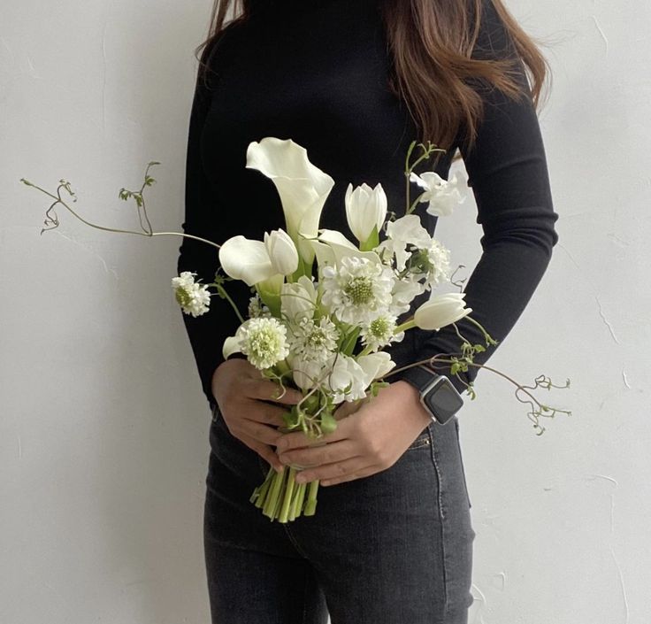 a woman holding a bouquet of white flowers in her right hand and wearing a black turtle neck sweater